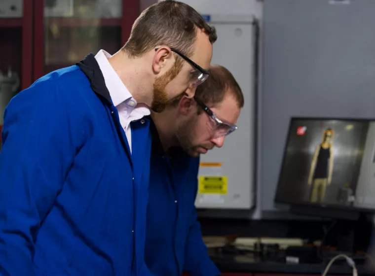 Two engineers in safety glasses engaged in a battery performance test. Exponent engineers assist with battery safety and recall support