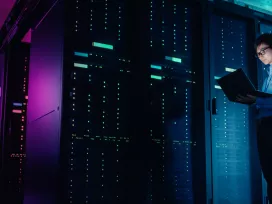 A person standing near a wall of servers. Exponent provides independent assessments of all types of computing systems.