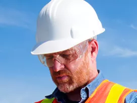 man in construction hat and vest looking down at clipboard