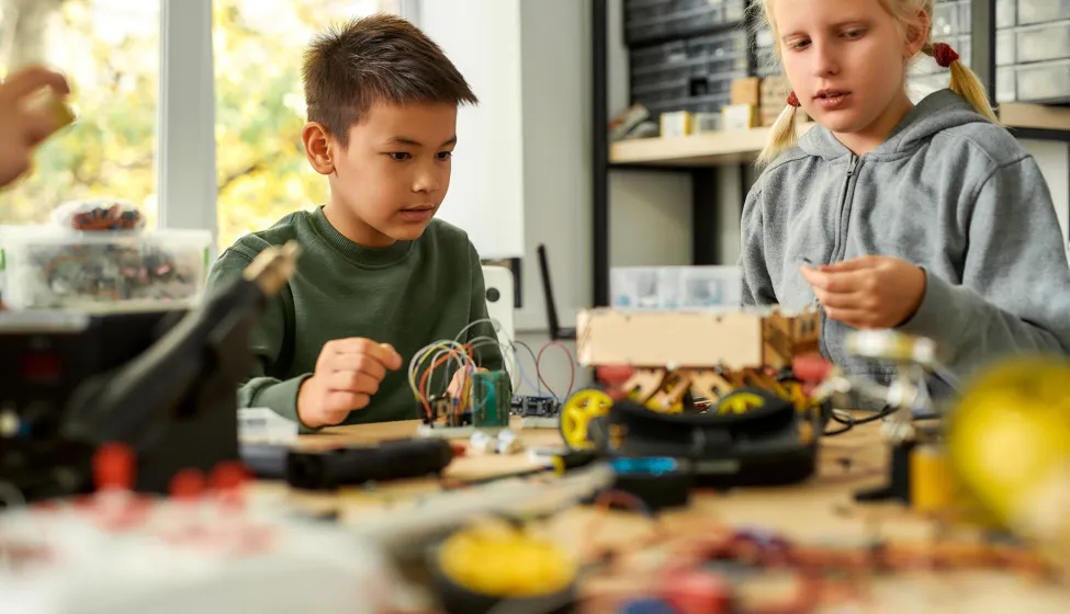 Asian boy and caucasian girl making their own vehicles at a stem robotics class. Inventions and creativity for children. Science and people concept.