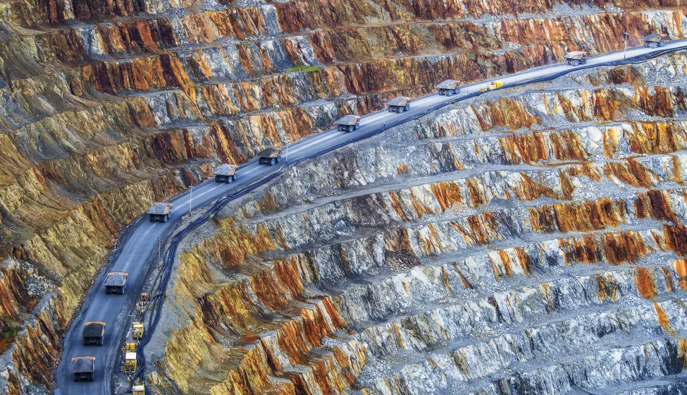 convoy of dump trucks driving through a mining operations area