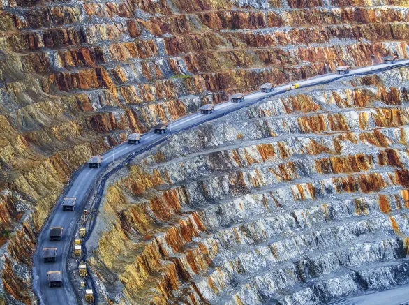 convoy of dump trucks driving through a mining operations area