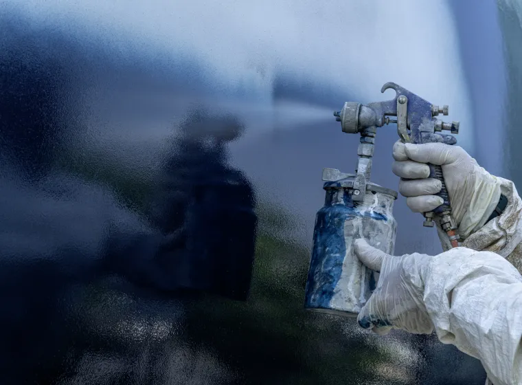 A worker in a body protective suit paints the hull of a sailing yacht with spray