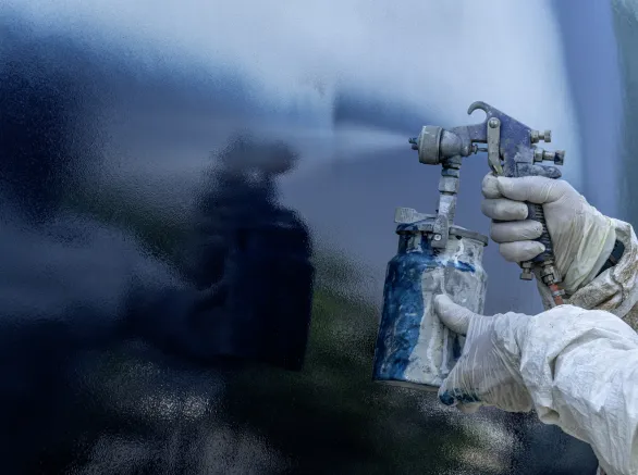 A worker in a body protective suit paints the hull of a sailing yacht with spray