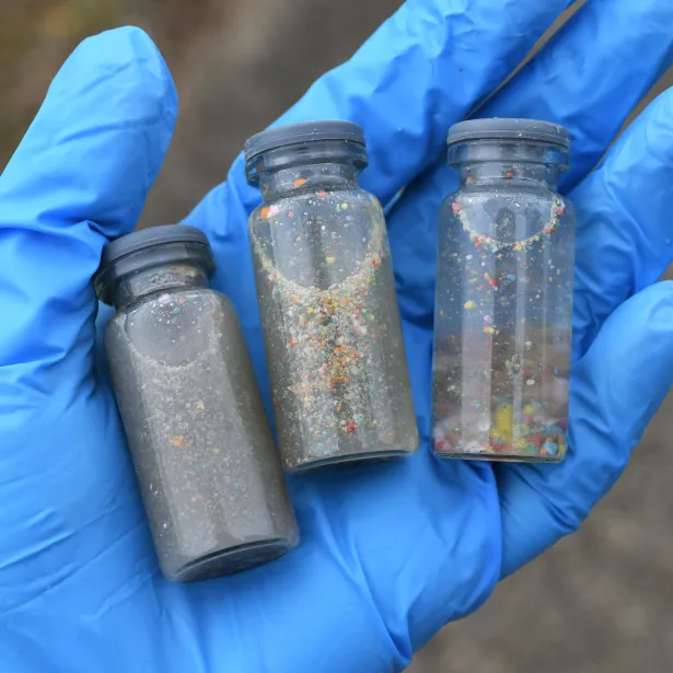 A gloved hand holding vials of water samples to test for pollution and plastic contamination