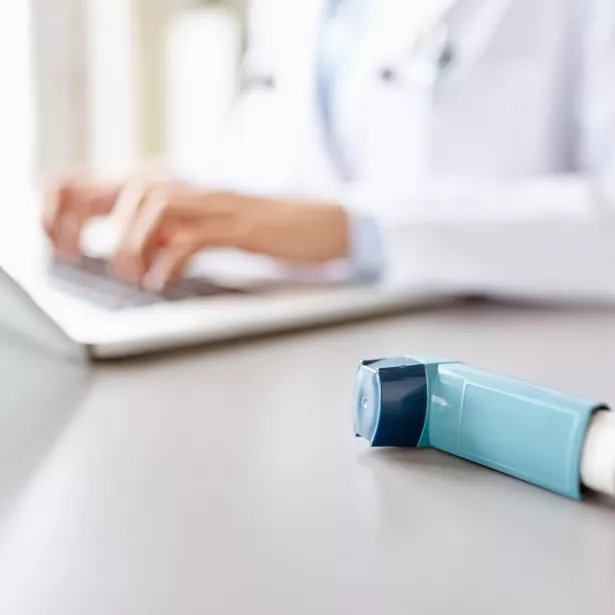 Inhaler on a desk with a medical professional using a laptop in the background