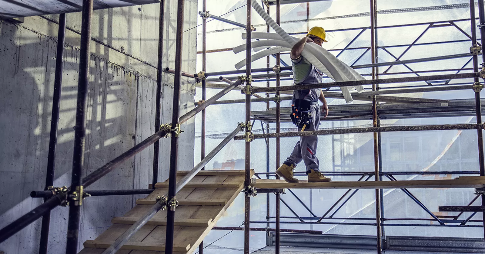 Worker balances PVC pipe while walking on scaffolding at a construction site. Exponent investigates construction accidents.