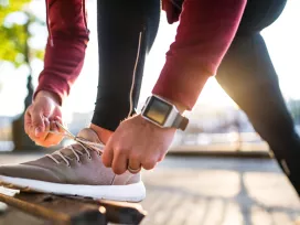 Close up of man in exercise clothing bending down to tie his shoe on a park bench